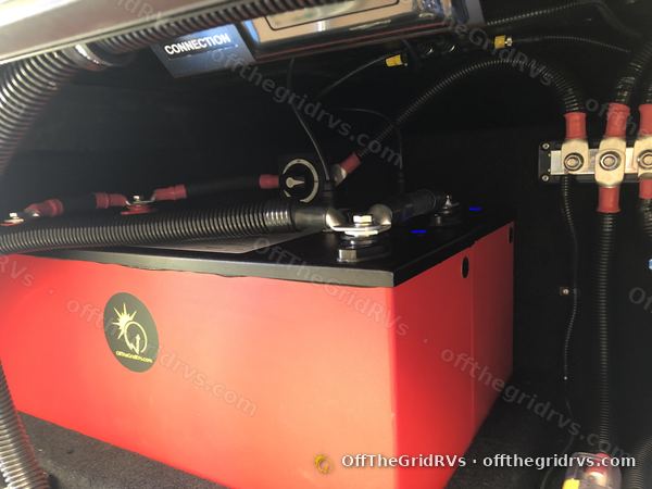 Close-up of a red Lithionics GTX12V320 battery in a Leisure Travel Vans Unity, with loomed cables running to red-capped busbars