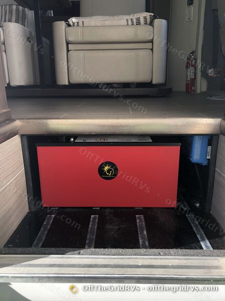 Red Lithionics GTX12V320 lithium battery installed under the open entry step of a Leisure Travel Vans Unity, with a blue Victron SmartSolar charge controller beside it
