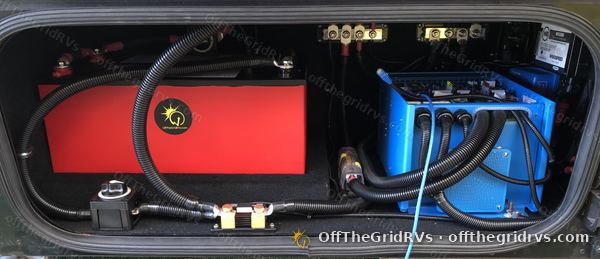 Open compartment to the left of the door on a Leisure Travel Vans Unity, with red Lithionics GTX12V320 batteries, a blue Victron MultiPlus 3000 inverter/charger, busbars and loomed cables