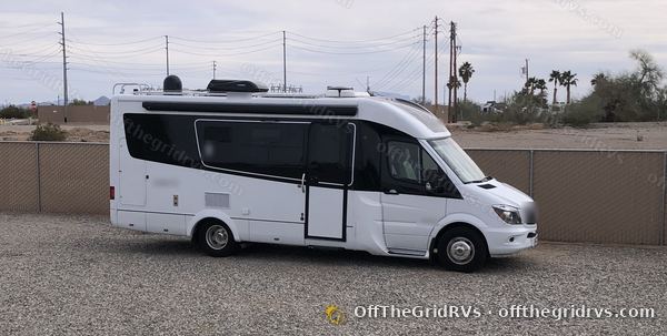 Side profile of the finished white Leisure Travel Vans Unity parked outdoors, with its roof solar panels lying flat and low