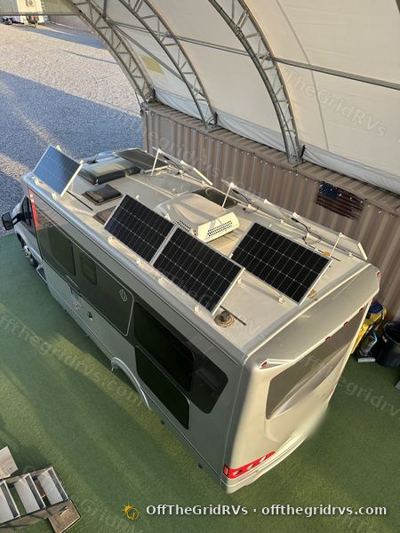Overhead view of eight 100W solar panels on manual tilt brackets laid out around the air conditioner and roof vents of a Leisure Travel Vans Unity