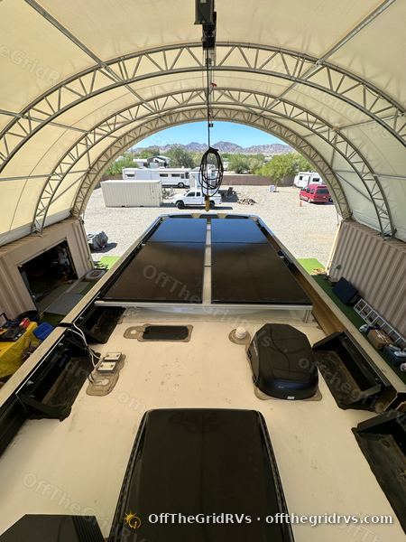 Solar panels on a bracket frame across an RV roof under the OffTheGridRVs shop canopy