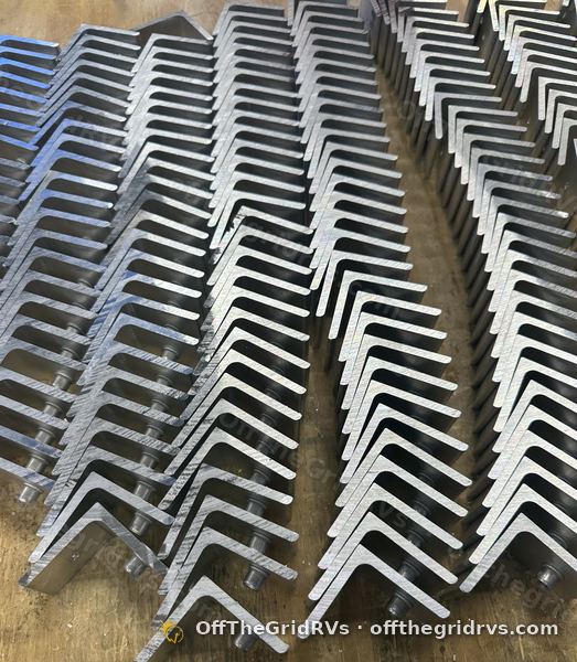 Overhead view of rows of finished aluminum tilt brackets on the OffTheGridRVs shop bench